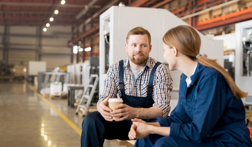 Two colleagues discussing in a grey board production workshop one holding a hot drink highlighting collaboration in eco friendly packaging manufacturing