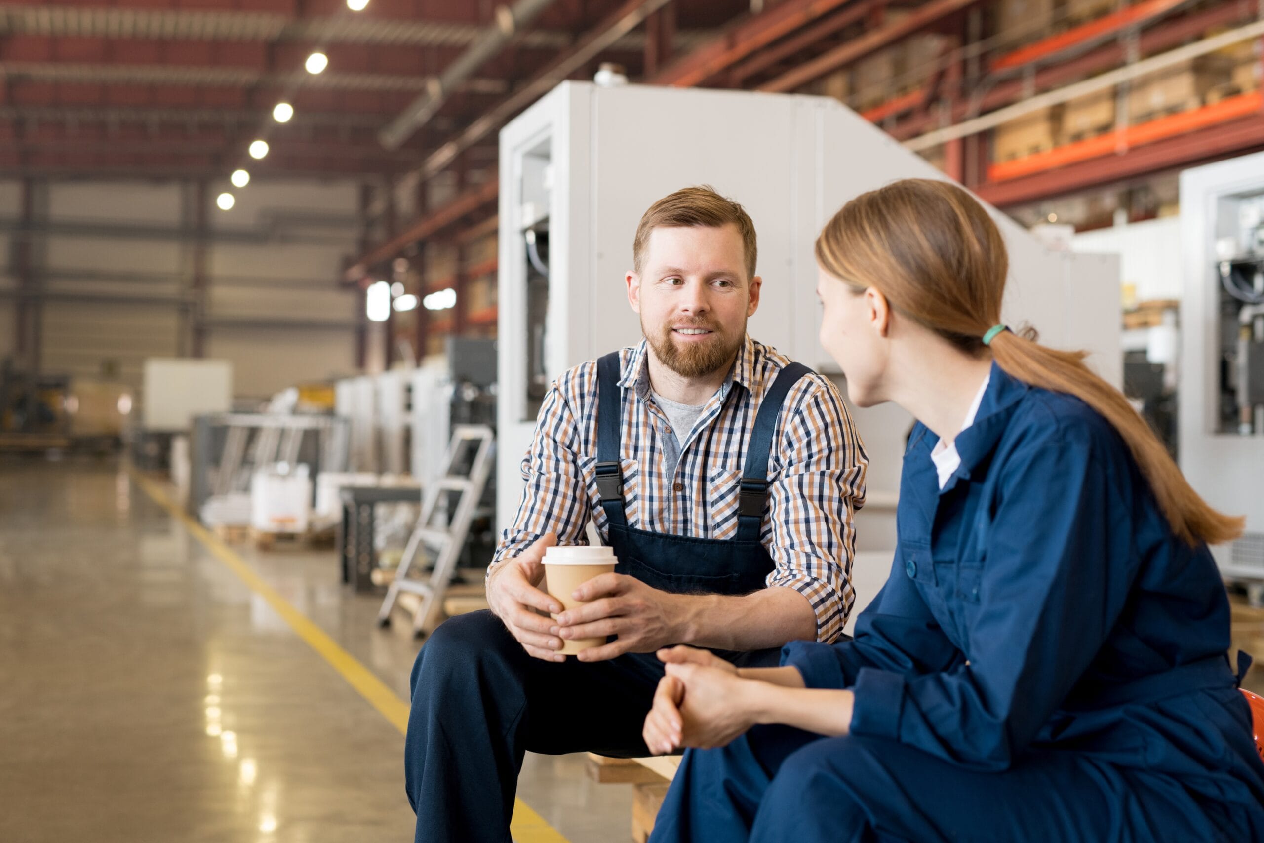 Two colleagues discussing in a grey board production workshop one holding a hot drink highlighting collaboration in eco friendly packaging manufacturing