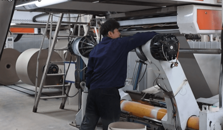 Worker operating greyboard manufacturing machine in packaging production line for rigid box board material