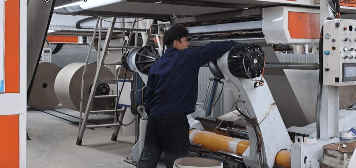 Worker operating greyboard manufacturing machine in packaging production line for rigid box board material