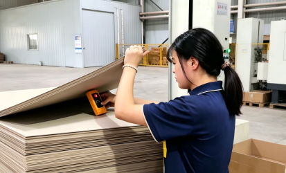 Worker measuring moisture content of grey board during packaging material quality inspection