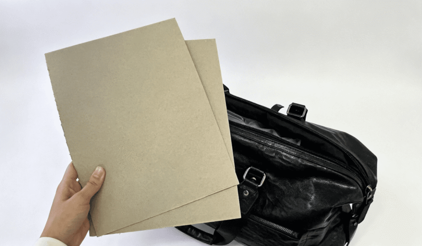 Greyboard sheets displayed next to black travel bag, greyboard material for bag stiffener