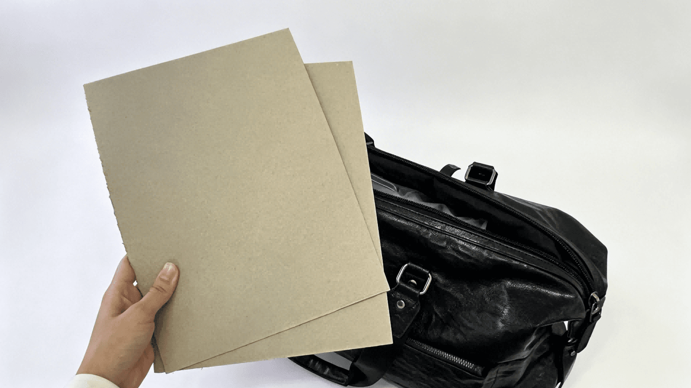 Greyboard sheets displayed next to black travel bag, greyboard material for bag stiffener